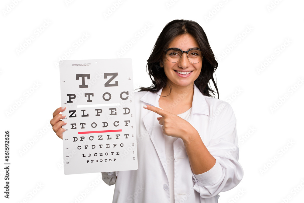 Young indian oculist woman holding an eye chart paper cut out isolated smiling and pointing aside, showing something at blank space. Young indian oculist woman holding an eye chart paper cut out isolated smiling and pointing aside, showing something at blank space.