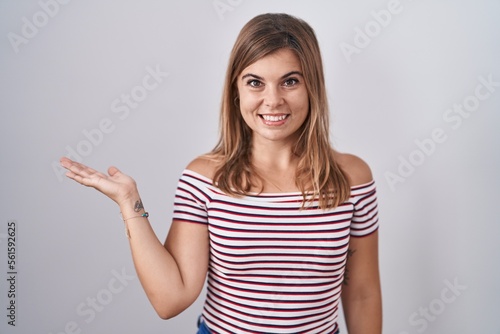 Wallpaper Mural Young hispanic woman standing over isolated background smiling cheerful presenting and pointing with palm of hand looking at the camera. Torontodigital.ca