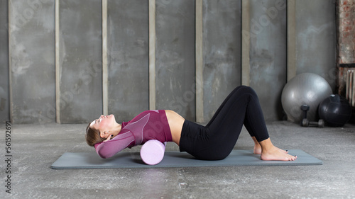 Foto A woman performs a myofascial release for her back using a roll on a yoga mat
