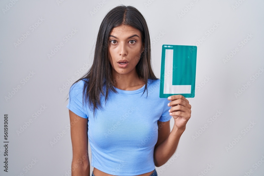 Brunette young woman holding l sign for new driver scared and amazed with open mouth for surprise, disbelief face Brunette young woman holding l sign for new driver scared and amazed with open mouth for surprise, disbelief face