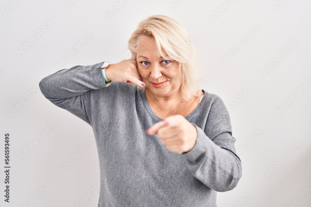 Middle age caucasian woman standing over white background smiling doing talking on the telephone gesture and pointing to you. call me. Middle age caucasian woman standing over white background smiling doing talking on the telephone gesture and pointing to you. call me.