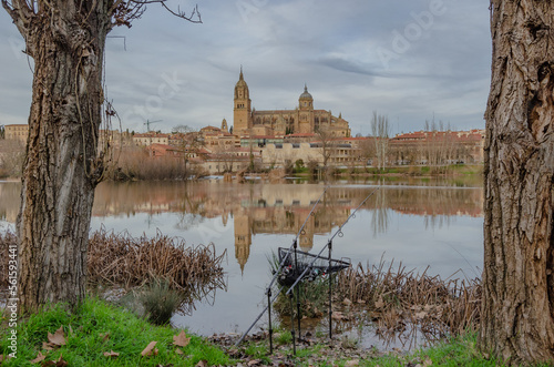 Catedral de Salamanca reflejada en el río Tormes vista entre dos arboles y dos cañas de pescar photo