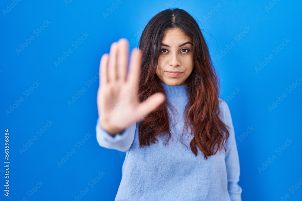 Fototapeta premium Hispanic young woman standing over blue background doing stop sing with palm of the hand. warning expression with negative and serious gesture on the face.
