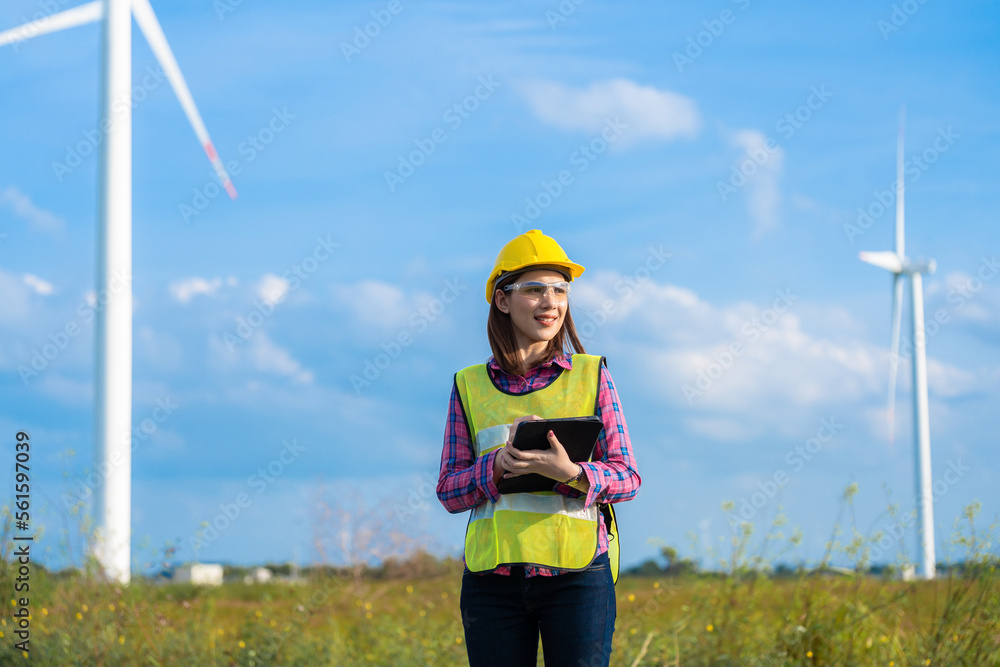 Female engineer or architect standing near electric turbine smart beautiful smile Wear a helmet and a vest. holding tablet ready to work close to the natural environment beautiful sky.