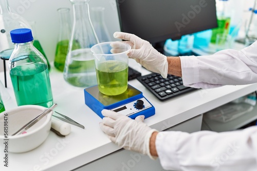 Senior grey-haired woman wearing scientist uniform weighing liquid at laboratory