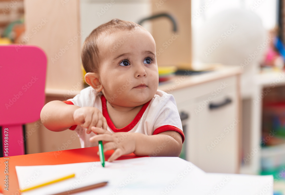 Adorable hispanic baby preschool student drawing on notebook standing at kindergarten