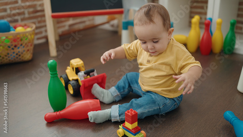 Adorable hispanic baby playing with construction blocks sitting on floor at kindergarten