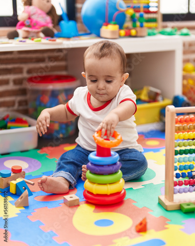 Adorable hispanic baby playing with abacus and hoops game sitting on floor at kindergarten