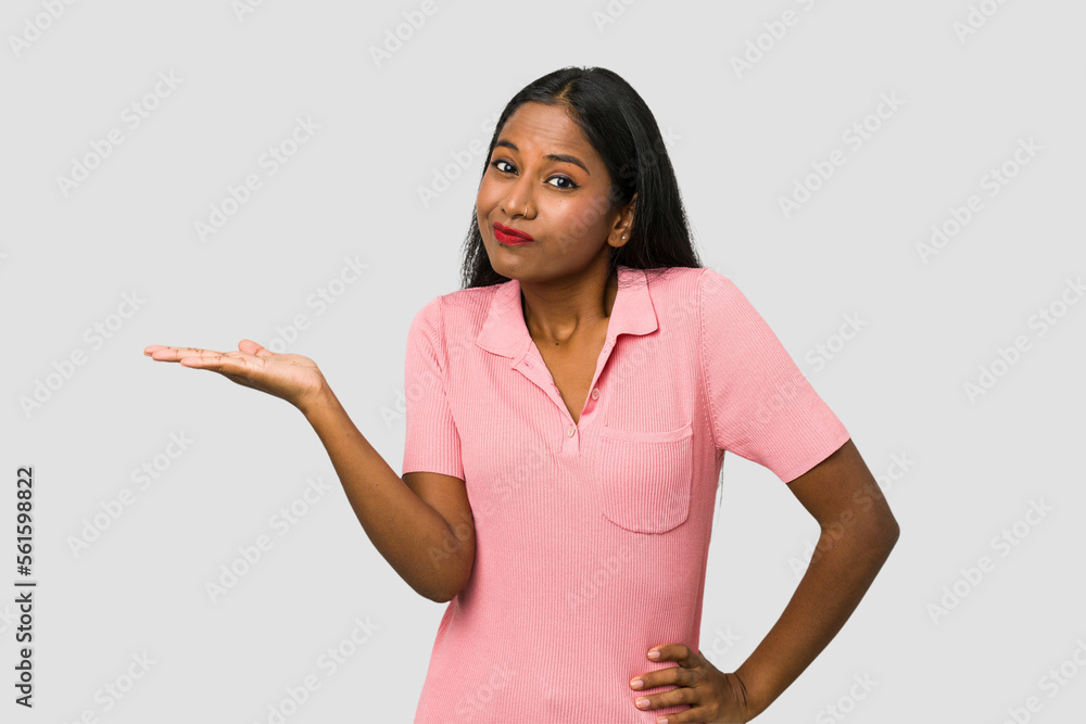 Young Indian woman cut out isolated on white background showing a copy space on a palm and holding another hand on waist. Young Indian woman cut out isolated on white background showing a copy space on a palm and holding another hand on waist.