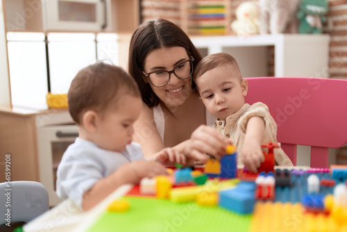 Teacher and preschool students playing with construction blocks sitting on table at kindergarten