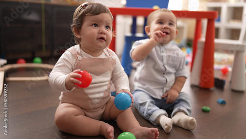 Two toddlers playing with balls sitting on floor at kindergarten