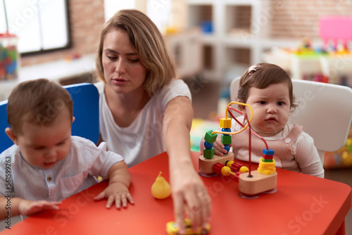 Teacher and preschool students playing with toys sitting on table at kindergarten