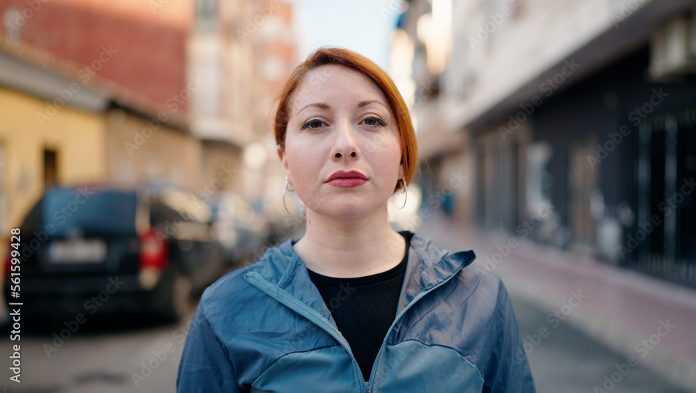 Young redhead woman wearing sportswear standing with relaxed expression at street