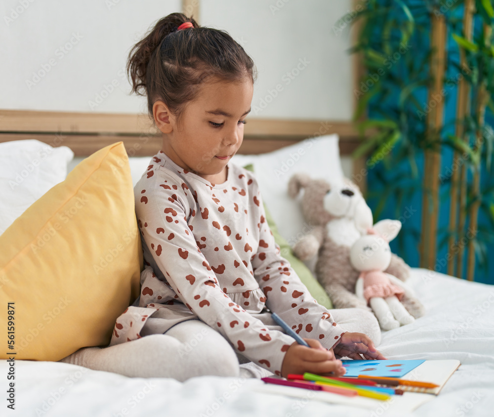 Fototapeta premium Adorable hispanic girl drawing on notebook sitting on bed at bedroom