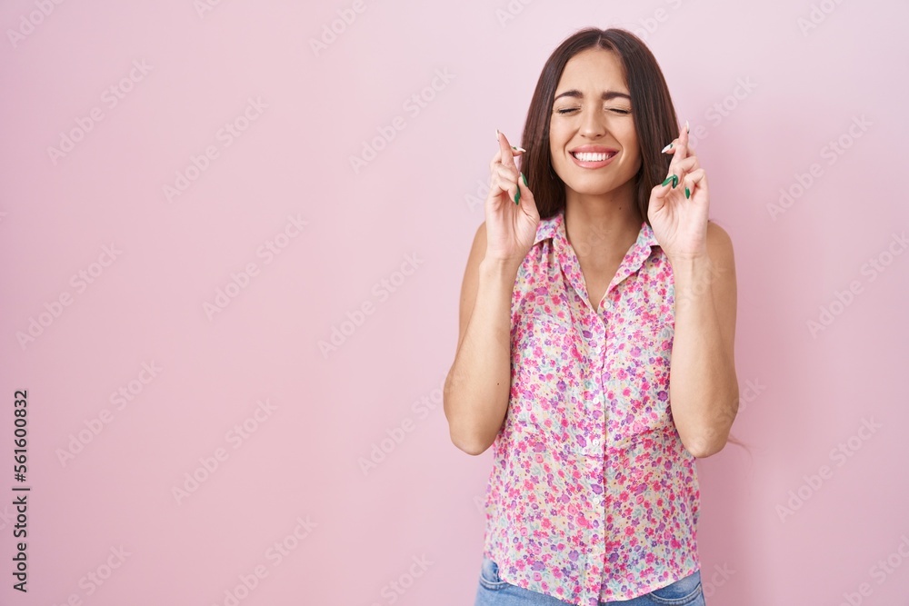 Young hispanic woman with long hair standing over pink background gesturing finger crossed smiling with hope and eyes closed. luck and superstitious concept. Young hispanic woman with long hair standing over pink background gesturing finger crossed smiling with hope and eyes closed. luck and superstitious concept.