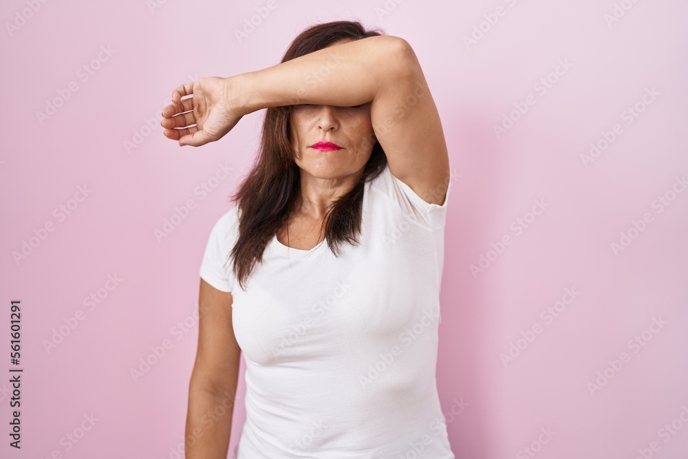 Middle age brunette woman standing over pink background covering eyes with arm, looking serious and sad. sightless, hiding and rejection concept Middle age brunette woman standing over pink background covering eyes with arm, looking serious and sad. sightless, hiding and rejection concept