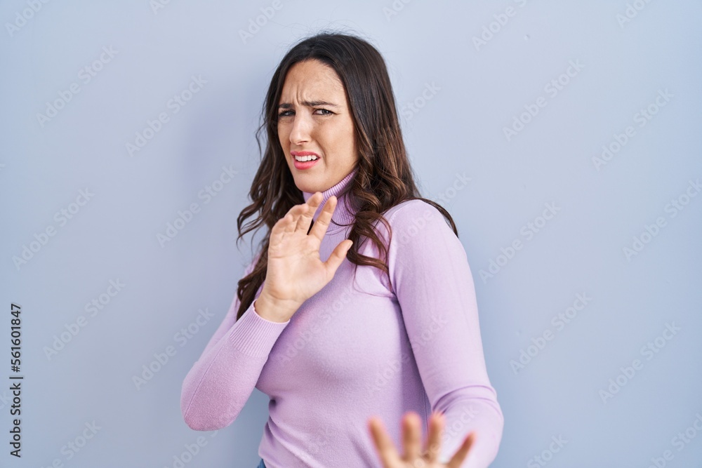 Young brunette woman standing over blue background disgusted expression, displeased and fearful doing disgust face because aversion reaction. Young brunette woman standing over blue background disgusted expression, displeased and fearful doing disgust face because aversion reaction.