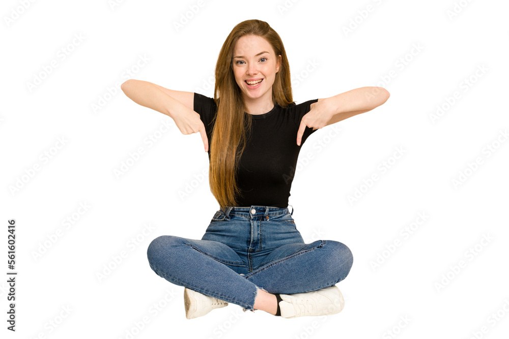 Young redhead woman sitting on the floor cut out isolated points down with fingers, positive feeling. Young redhead woman sitting on the floor cut out isolated points down with fingers, positive feeling.