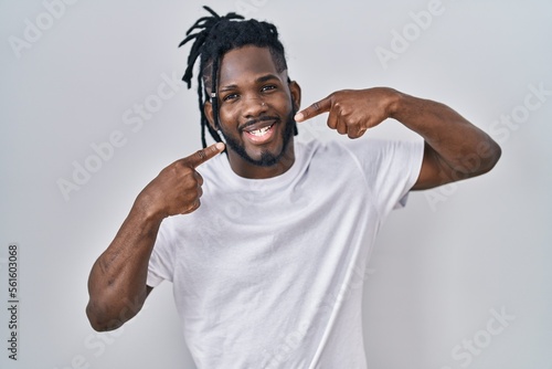 African man with dreadlocks wearing casual t shirt over white background smiling cheerful showing and pointing with fingers teeth and mouth. dental health concept.