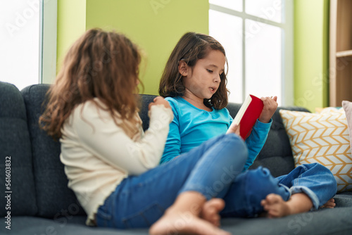 Two kids reading book sitting on sofa at home