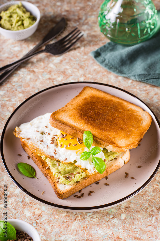 Fried egg, avocado and flax seeds on fried bread on a plate on the table. Vertical view