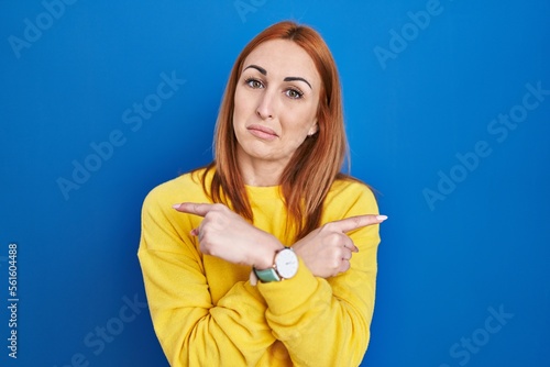 Young woman standing over blue background pointing to both sides with fingers, different direction disagree