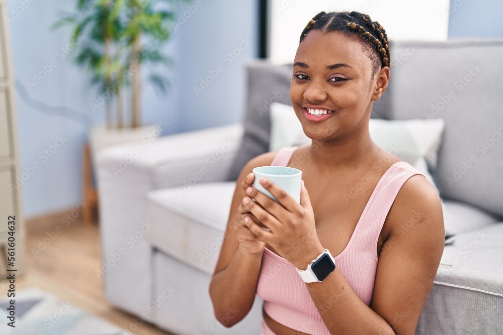African american woman drinking coffee sitting on floor at home