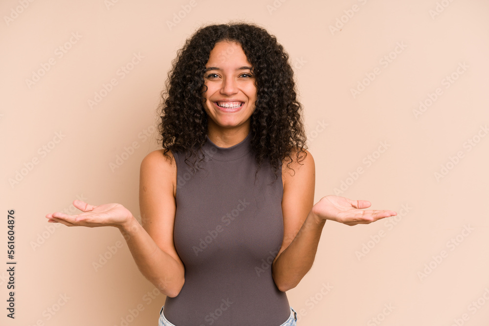 Young african american curly woman isolated makes scale with arms, feels happy and confident. Young african american curly woman isolated makes scale with arms, feels happy and confident.