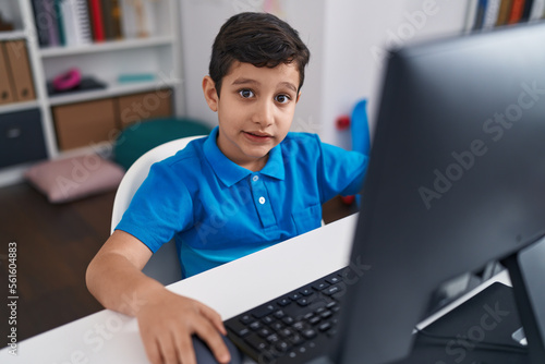 Adorable hispanic boy student using computer sitting on table at classroom