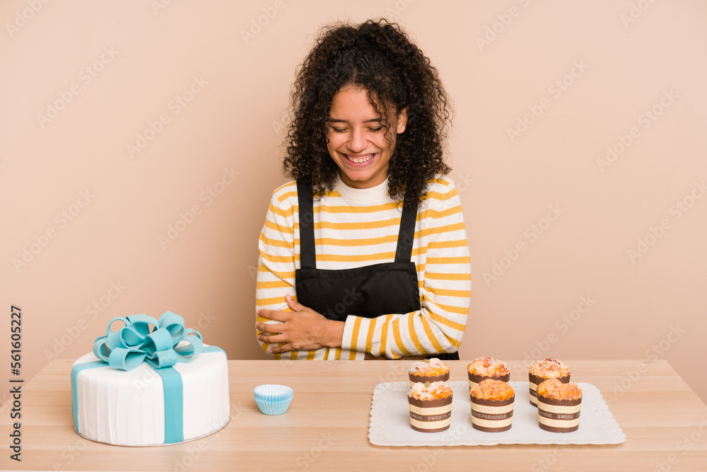 Young african american woman preparing a sweet cake and muffins on a table laughing and having fun. Young african american woman preparing a sweet cake and muffins on a table laughing and having fun.