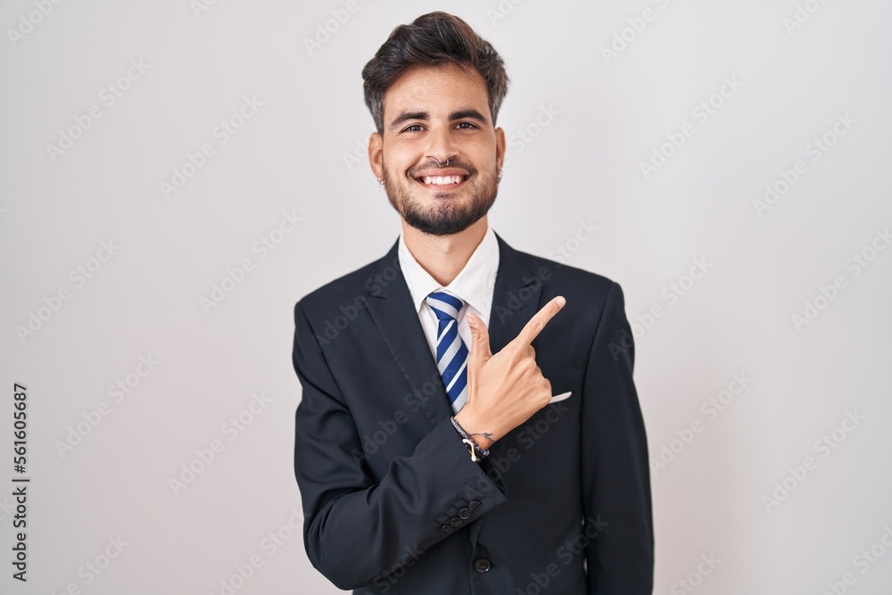 Young hispanic man with tattoos wearing business suit and tie cheerful with a smile on face pointing with hand and finger up to the side with happy and natural expression Young hispanic man with tattoos wearing business suit and tie cheerful with a smile on face pointing with hand and finger up to the side with happy and natural expression