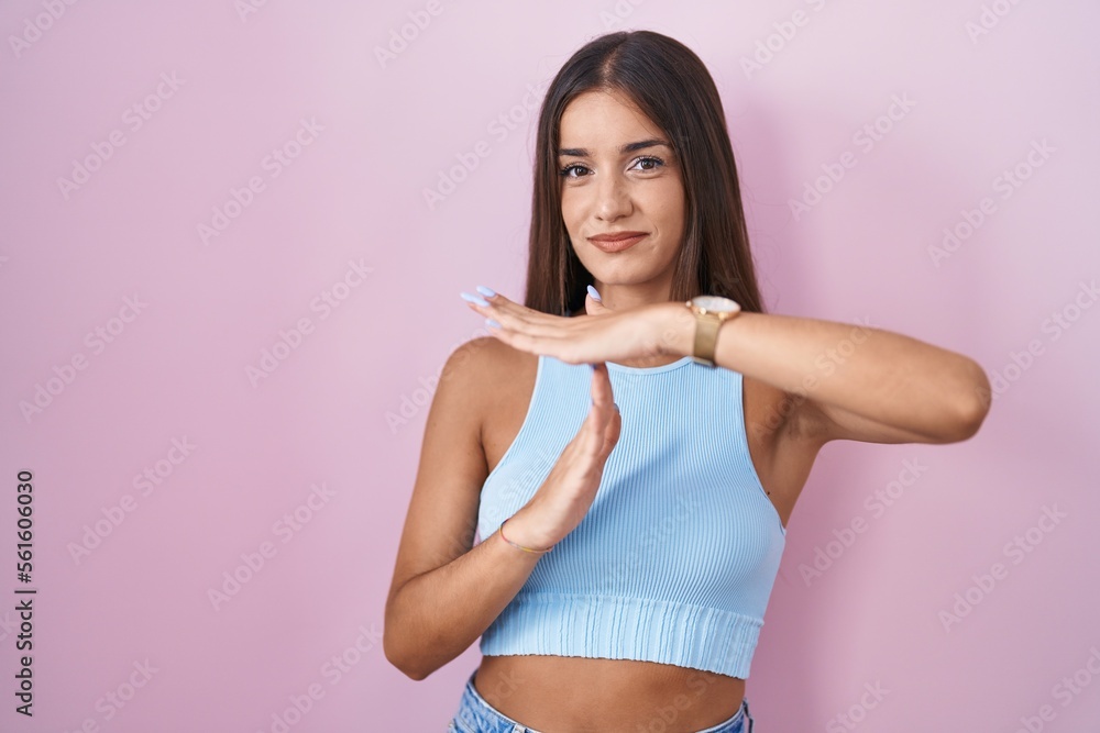 Young brunette woman standing over pink background doing time out gesture with hands, frustrated and serious face Young brunette woman standing over pink background doing time out gesture with hands, frustrated and serious face