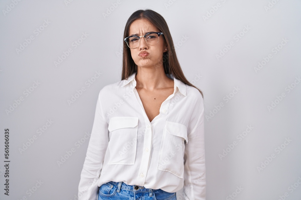 Young brunette woman wearing glasses puffing cheeks with funny face. mouth inflated with air, crazy expression. Young brunette woman wearing glasses puffing cheeks with funny face. mouth inflated with air, crazy expression.