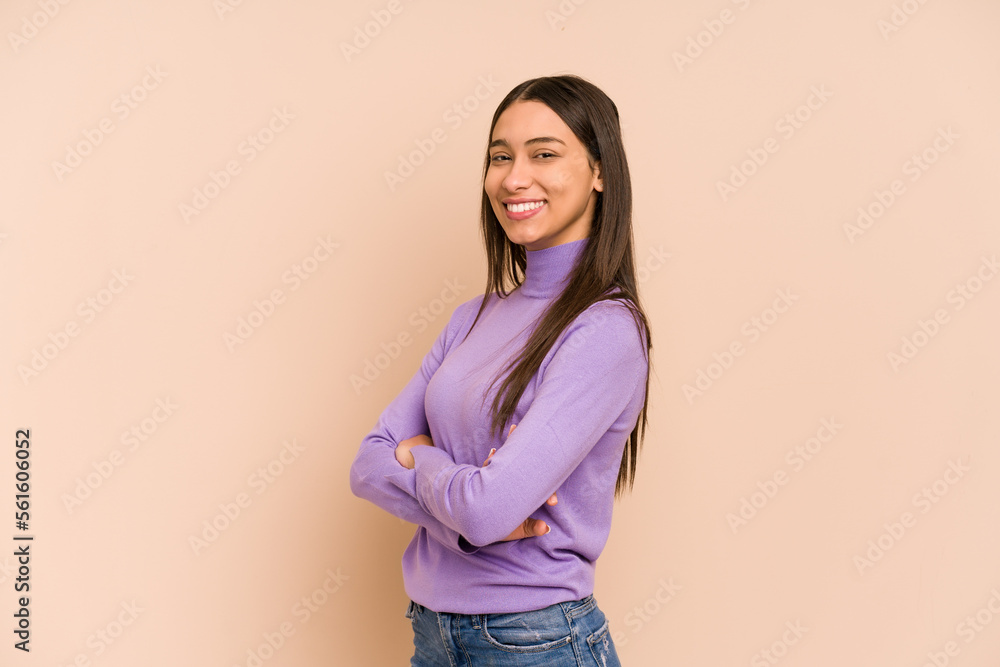 Young colombian woman isolated on beige background who feels confident, crossing arms with determination. Young colombian woman isolated on beige background who feels confident, crossing arms with determination.