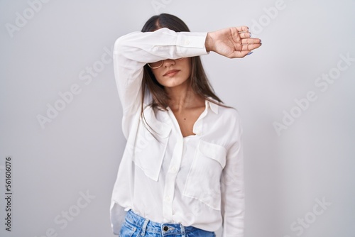Young brunette woman wearing glasses covering eyes with arm, looking serious and sad. sightless, hiding and rejection concept