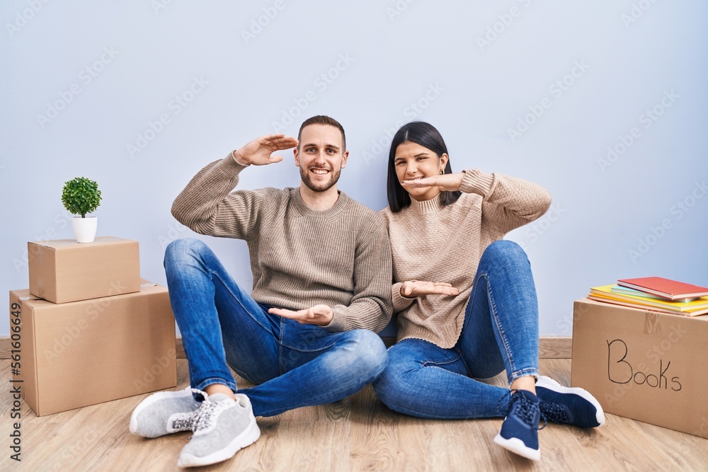 Young couple moving to a new home gesturing with hands showing big and large size sign, measure symbol. smiling looking at the camera. measuring concept. Young couple moving to a new home gesturing with hands showing big and large size sign, measure symbol. smiling looking at the camera. measuring concept.