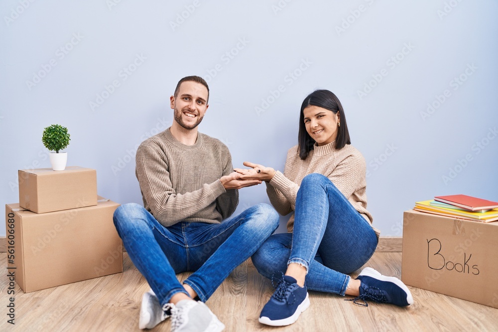 Young couple moving to a new home pointing aside with hands open palms showing copy space, presenting advertisement smiling excited happy Young couple moving to a new home pointing aside with hands open palms showing copy space, presenting advertisement smiling excited happy