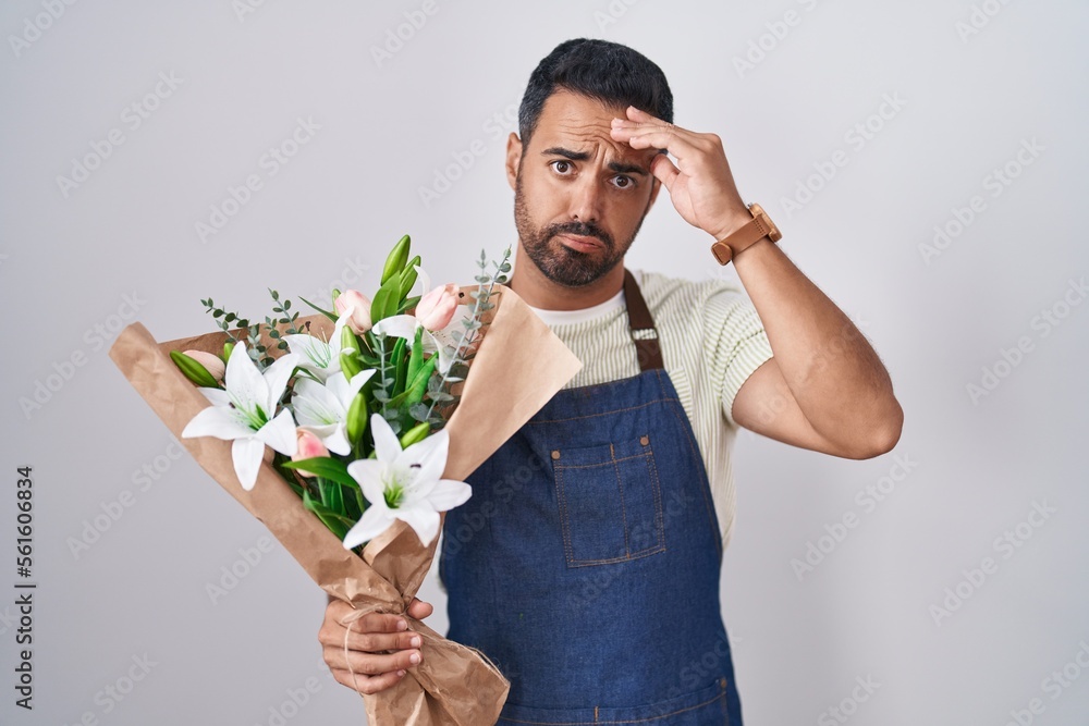 Hispanic man with beard working as florist worried and stressed about a problem with hand on forehead, nervous and anxious for crisis Hispanic man with beard working as florist worried and stressed about a problem with hand on forehead, nervous and anxious for crisis