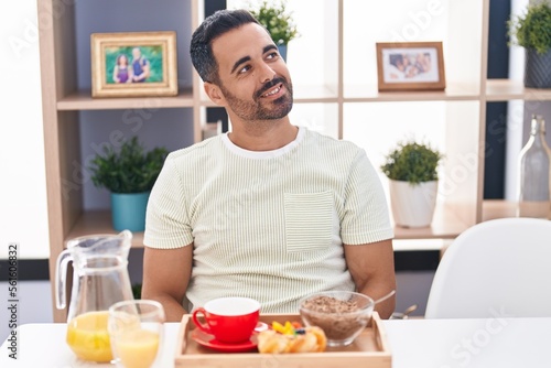 Hispanic man with beard eating breakfast looking to side  relax profile pose with natural face and confident smile.
