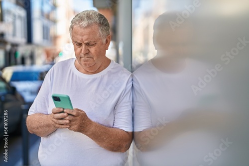 Middle age grey-haired man using smartphone with relaxed expression at street © Krakenimages.com