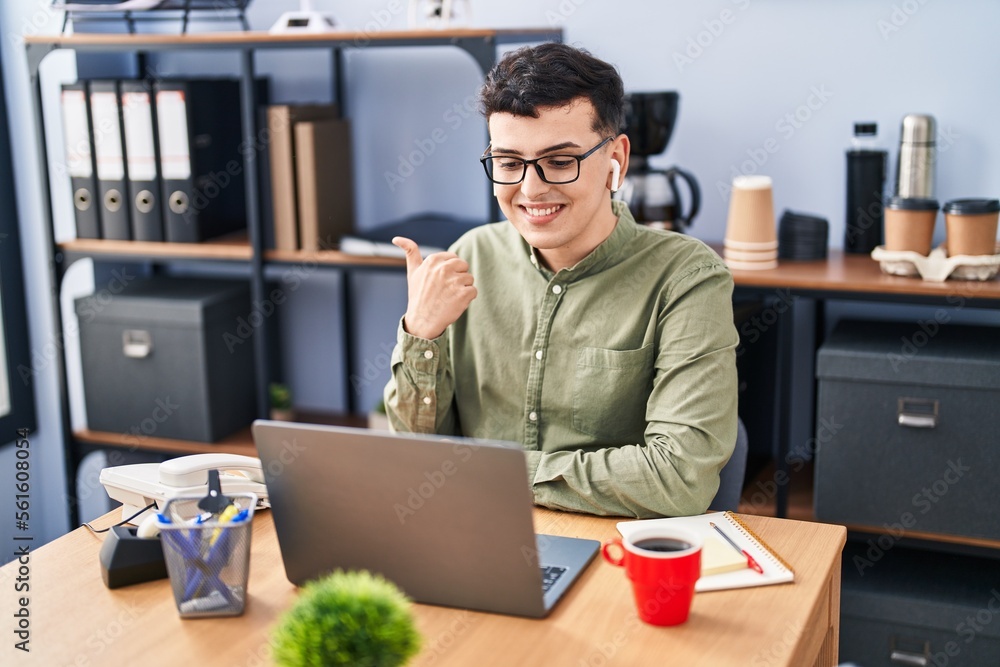 Non binary person working at the office wearing glasses pointing thumb up to the side smiling happy with open mouth Non binary person working at the office wearing glasses pointing thumb up to the side smiling happy with open mouth