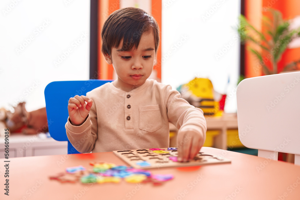 Adorable hispanic boy playing with maths puzzle game sitting on table at kindergarten Adorable hispanic boy playing with maths puzzle game sitting on table at kindergarten