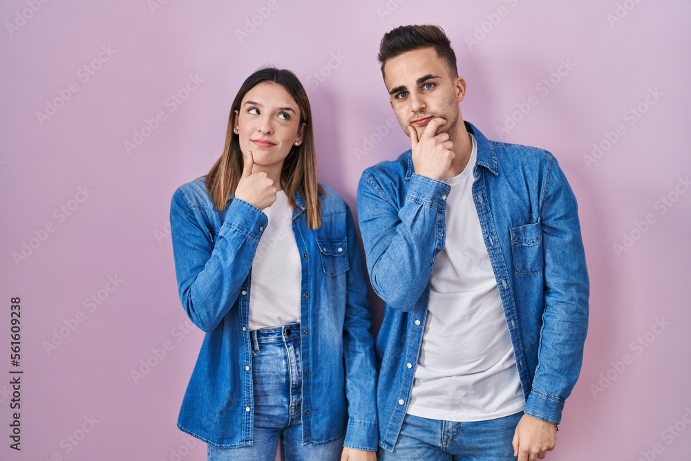 Young hispanic couple standing over pink background looking confident at the camera smiling with crossed arms and hand raised on chin. thinking positive. Young hispanic couple standing over pink background looking confident at the camera smiling with crossed arms and hand raised on chin. thinking positive.