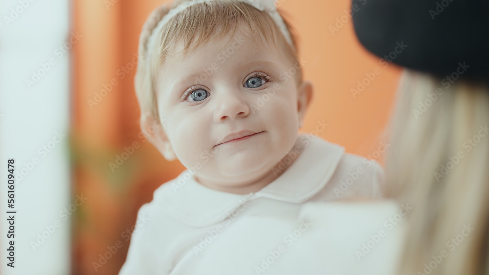 Adorable blonde baby smiling confident on mother arms at home