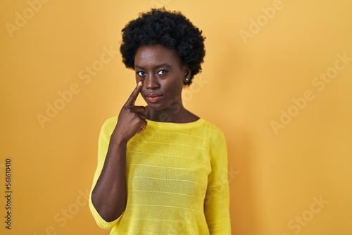 African young woman standing over yellow studio pointing to the eye watching you gesture, suspicious expression © Krakenimages.com