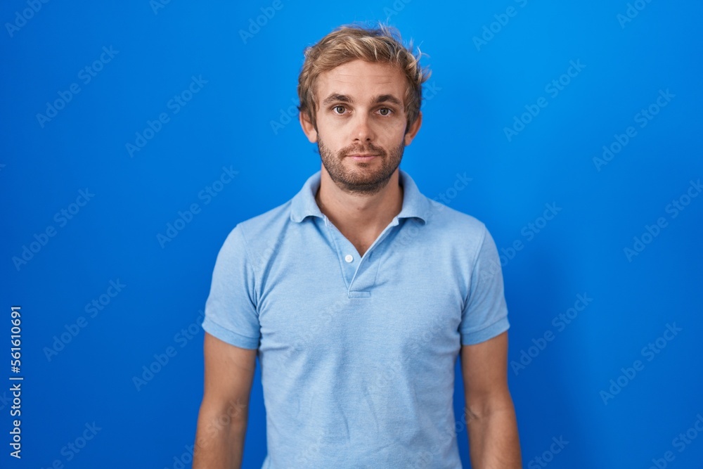 Caucasian man standing over blue background relaxed with serious expression on face. simple and natural looking at the camera. Caucasian man standing over blue background relaxed with serious expression on face. simple and natural looking at the camera.