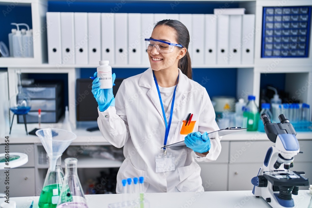 Young hispanic woman scientist holding pills at laboratory