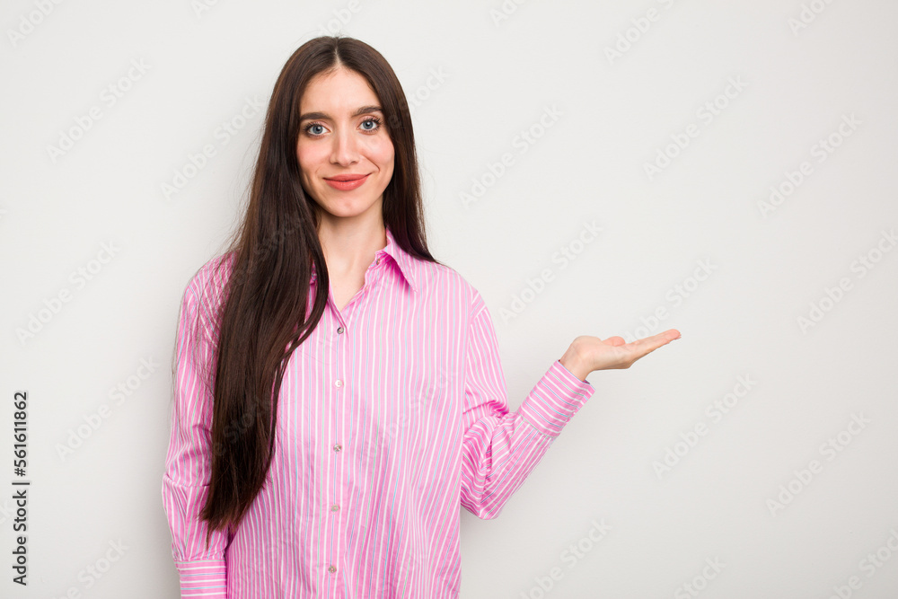 Young caucasian woman isolated on white background showing a copy space on a palm and holding another hand on waist. Young caucasian woman isolated on white background showing a copy space on a palm and holding another hand on waist.