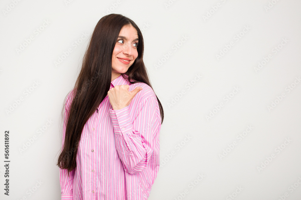 Young caucasian woman isolated on white background points with thumb finger away, laughing and carefree. Young caucasian woman isolated on white background points with thumb finger away, laughing and carefree.