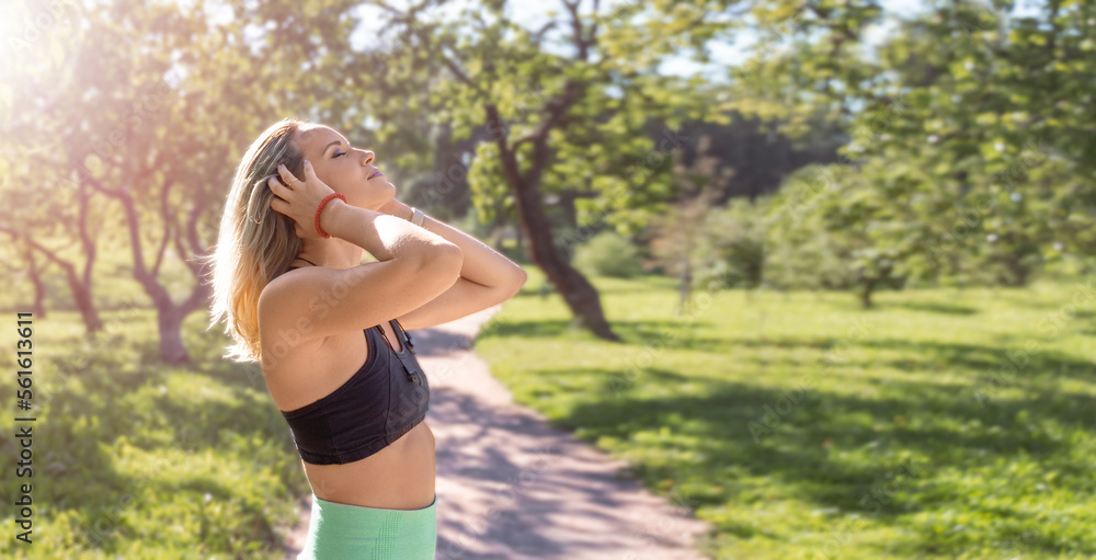 Caucasian middle-aged woman tie hair before workout exercise in public park in sunny summer morning. Warm up running jogging training. Active healthy lifestyle. Copy space banner Caucasian middle-aged woman tie hair before workout exercise in public park in sunny summer morning. Warm up running jogging training. Active healthy lifestyle. Copy space banner